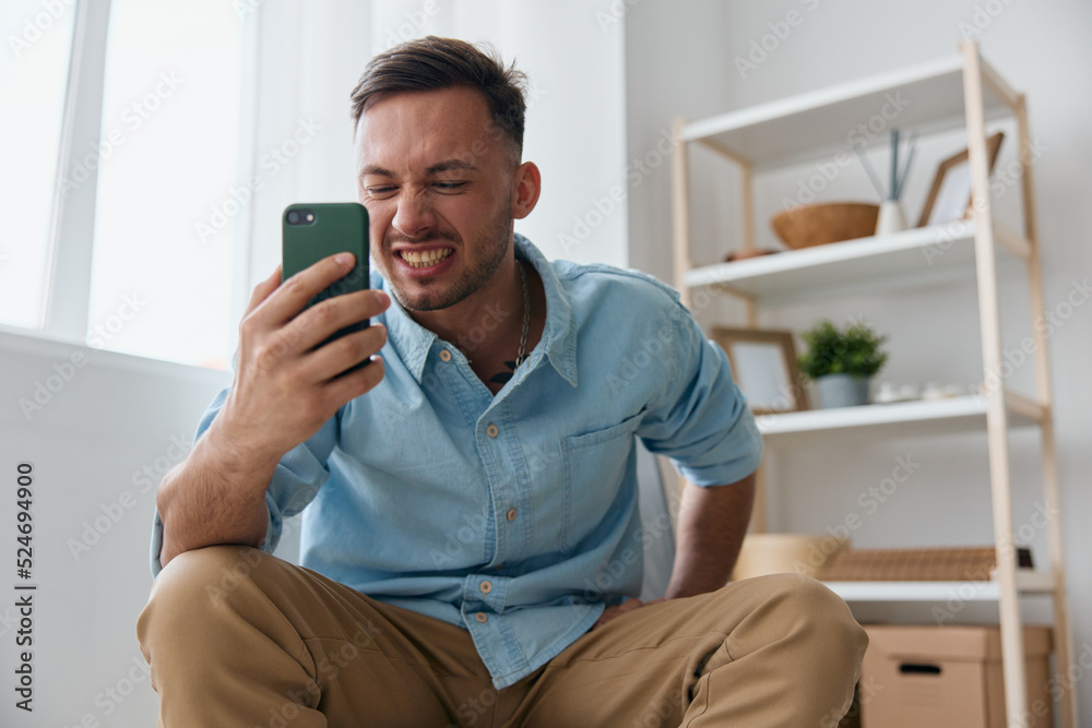 Angry irritated evil self-confident handsome man tells with someone using video call at phone sitting at home. Attractive guy hates operation mobile crash problems. Time to buy new device concept