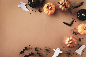 Halloween holiday frame with party decorations of pumpkins, bats, ghosts, spiders on golden background top view. Happy halloween greeting card in flat lay style.