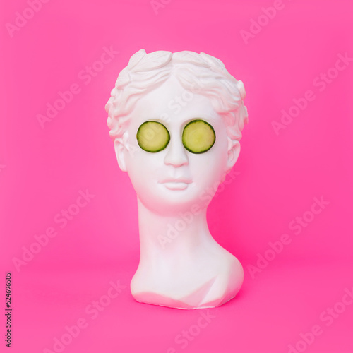 Antique female statue's head with cucumber slices on her eyes isolated on a pink background. 3d contemporary art. Modern design. Beauty concept