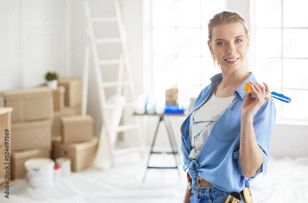 Pretty smilling woman painting interior wall of home with paint roller Pretty smilling woman painting interior wall of home with paint roller
