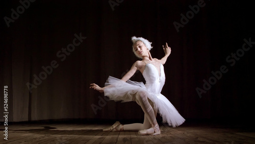 in rays of spotlight, on the stage of the old theater hall. Young ballerina in suit of white swan and pointe shoes, dances elegantly certain ballet motion, part de bras. High quality photo photo