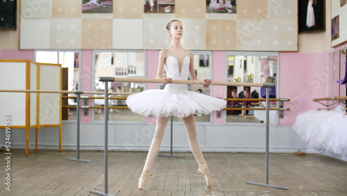 in the ballet hall, girl in white pack is engaged at the ballet, rehearse Roleve, goes up on toes, in pointe shoes , Young ballerina standing at railing in ballet hall. High quality photo photo