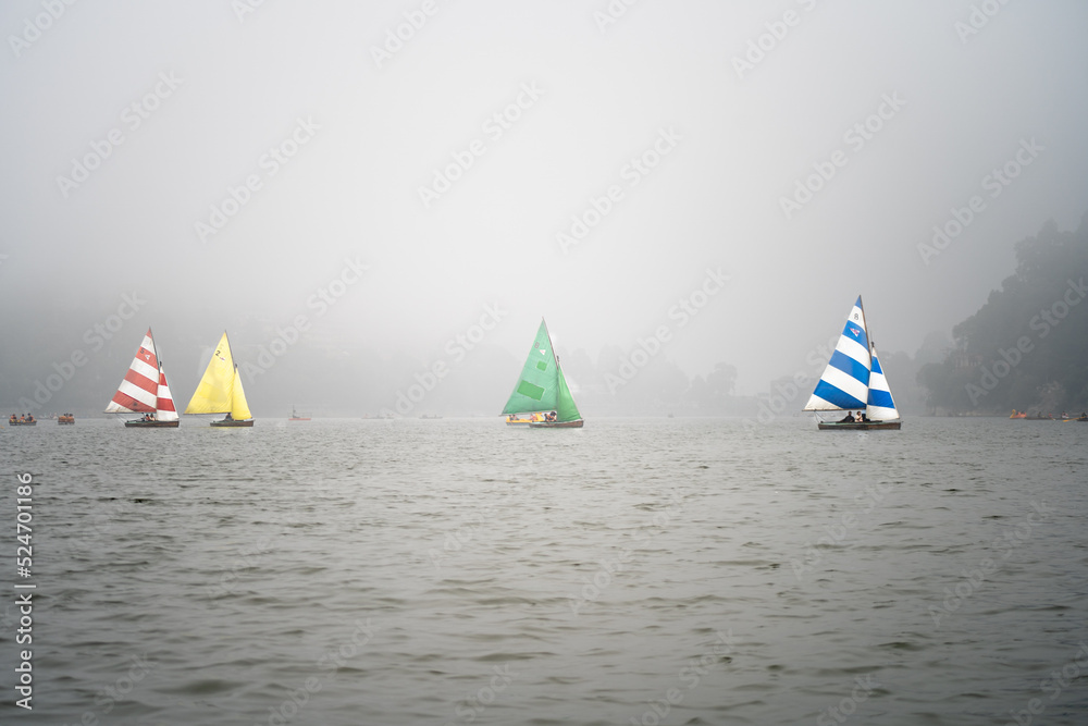 four colorful sailboats lost in the haze fog with smaller pedal row boats floating around on the