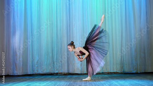 ballet rehearsal, on the stage of the old theater hall. Young ballerina in lilac black dress and pointe shoes, dances elegantly certain ballet motion, raises her leg up behind. High quality photo photo