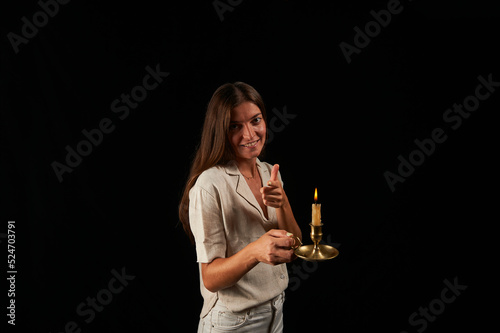 young woman lit by an old brass lamp with a candle on a black background points with her left hand