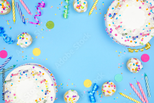 Birthday party frame on a blue background. Overhead view with cakes, party hats and confetti. Copy space.