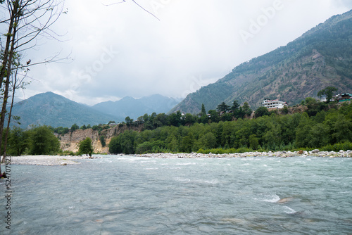 Scenic view of Beas river flowing in background of peaks of Himalayan mountains and dark clouds in sky at Manali, Himachal Pradesh, India. Mountain River. Travel in Himalayas. Natural landscape photo