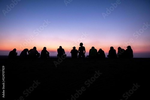A group of people, team work, companions, friends sitting together during sunrise or sunset, silhouette © dalia