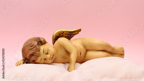 Fototapeta Naklejka Na Ścianę i Meble -  Figura de Angel de ceramica recostado y durmiendo sobre una cama blanca. 
