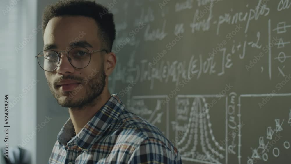 Chest up portrait shot of young biracial student posing for camera near chalkboard in college classroom Chest up portrait shot of young biracial student posing for camera near chalkboard in college classroom