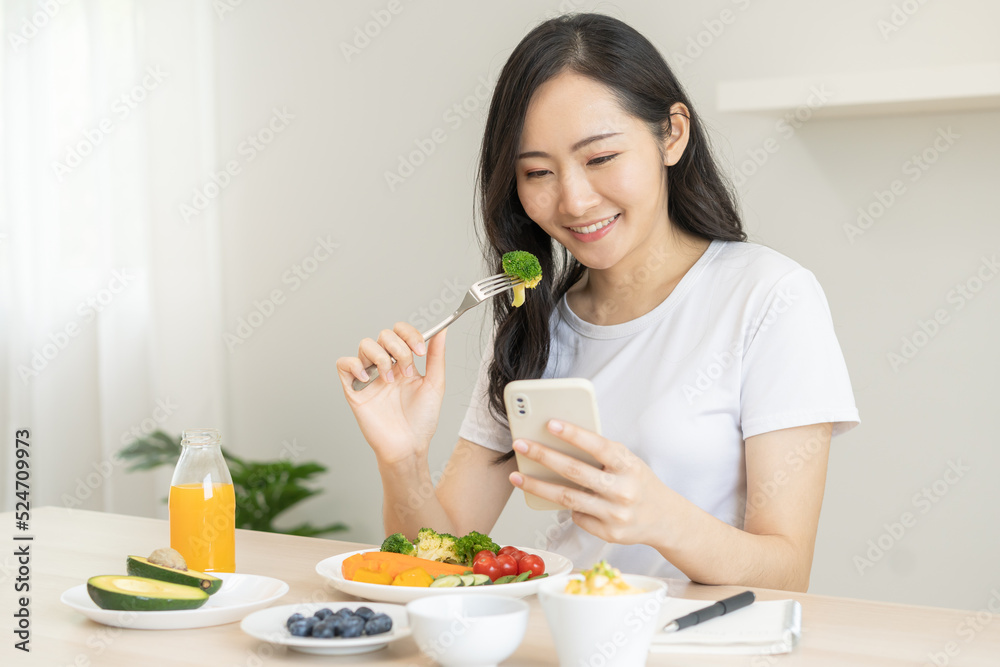 Dieting, asian young woman eating, holding fork at broccoli, diet plan nutrition with fresh vegetables salad, enjoy meal while using smartphone. Nutritionist of healthy, nutrition of weight loss. Dieting, asian young woman eating, holding fork at broccoli, diet plan nutrition with fresh vegetables salad, enjoy meal while using smartphone. Nutritionist of healthy, nutrition of weight loss.