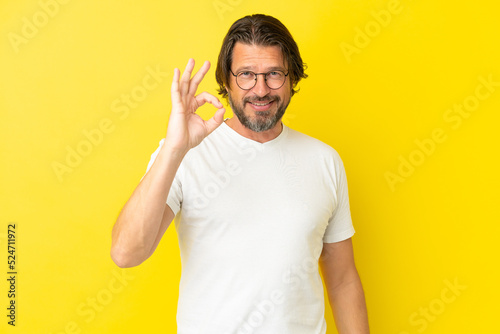 Senior dutch man isolated on yellow background showing ok sign with fingers