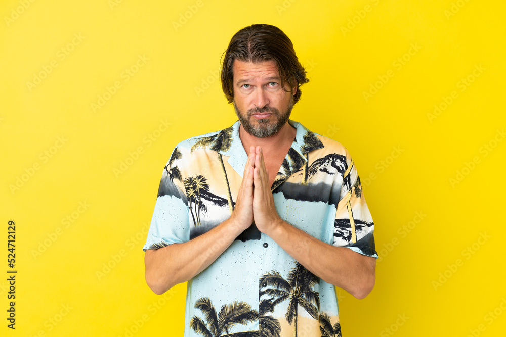 Senior dutch man isolated on yellow background keeps palm together. Person asks for something Senior dutch man isolated on yellow background keeps palm together. Person asks for something