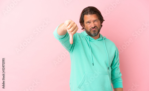 Senior dutch man isolated on pink background showing thumb down with negative expression
