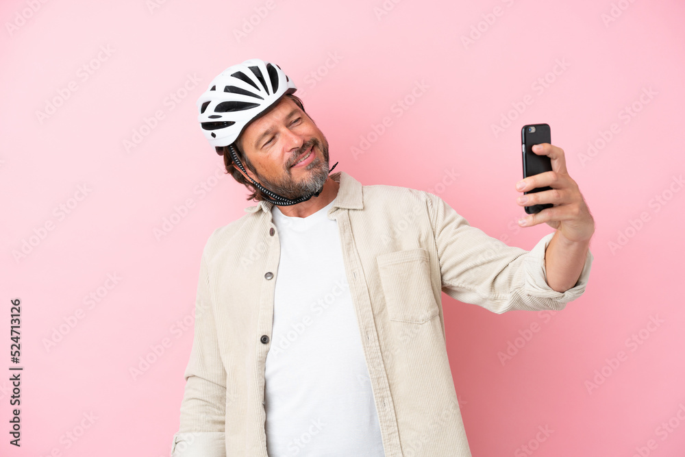Senior dutch man with bike helmet isolated on pink background making a selfie Senior dutch man with bike helmet isolated on pink background making a selfie