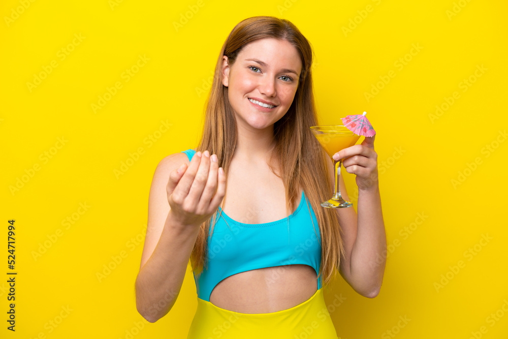 Young caucasian woman holding a cocktail isolated on yellow background inviting to come with hand. Happy that you came Young caucasian woman holding a cocktail isolated on yellow background inviting to come with hand. Happy that you came