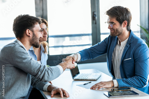 Attractive real-estate agent shaking hands with young couple after signing agreement contract in the office. photo