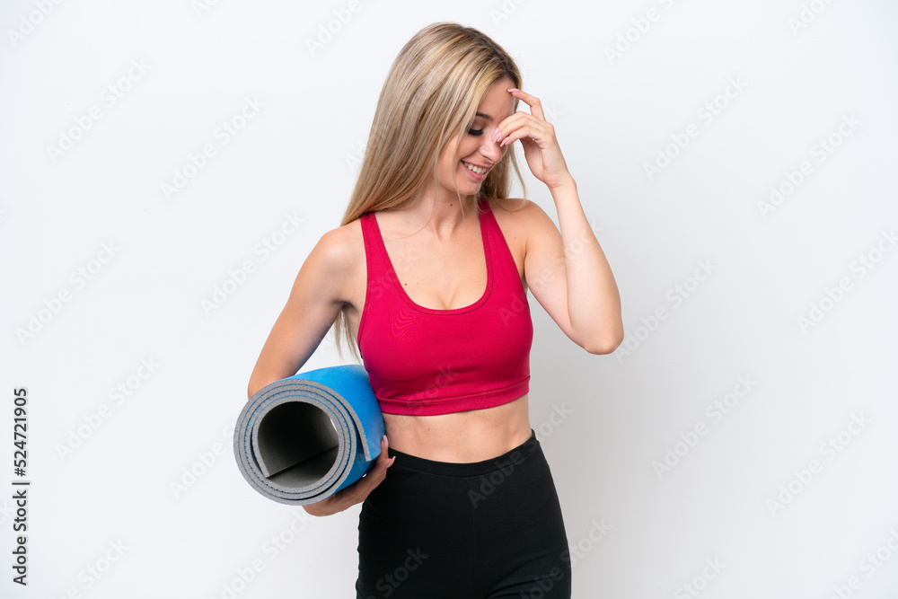 Young sport blonde woman going to yoga classes while holding a mat isolated on white background laughing Young sport blonde woman going to yoga classes while holding a mat isolated on white background laughing