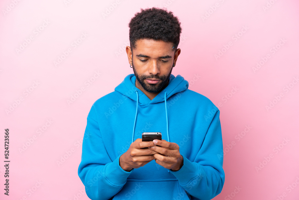 Young Brazilian man isolated on pink background using mobile phone Young Brazilian man isolated on pink background using mobile phone