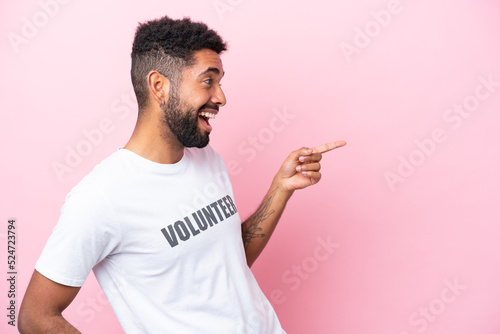 Young volunteer man isolated on pink background pointing finger to the side and presenting a product