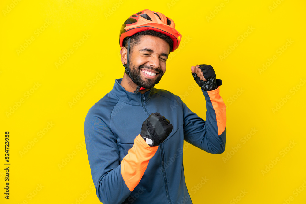 Young cyclist Brazilian man isolated on yellow background celebrating a victory Young cyclist Brazilian man isolated on yellow background celebrating a victory