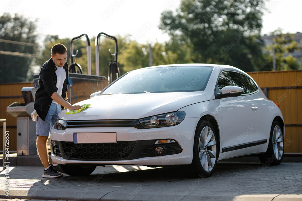Man is wiping the car with a microfiber cloth. Contactless self-service car wash. Personal car care cleaning outside. Concept disinfection and antiseptic cleaning of vehicle, covid-19 and coronavirus