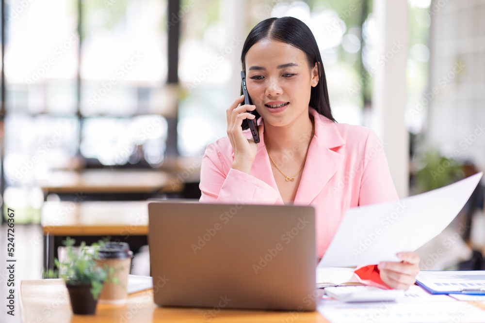 Young Business Asian woman talking on a smartphone and working in an office. Asian female Business finance sitting at his workplace. Young Business Asian woman talking on a smartphone and working in an office. Asian female Business finance sitting at his workplace.
