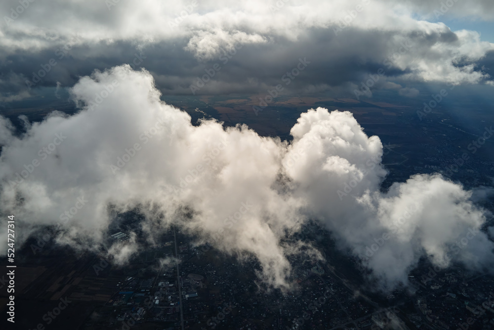 Aerial view from airplane window at high altitude of distant city covered with puffy cumulus clouds forming before rainstorm Aerial view from airplane window at high altitude of distant city covered with puffy cumulus clouds forming before rainstorm
