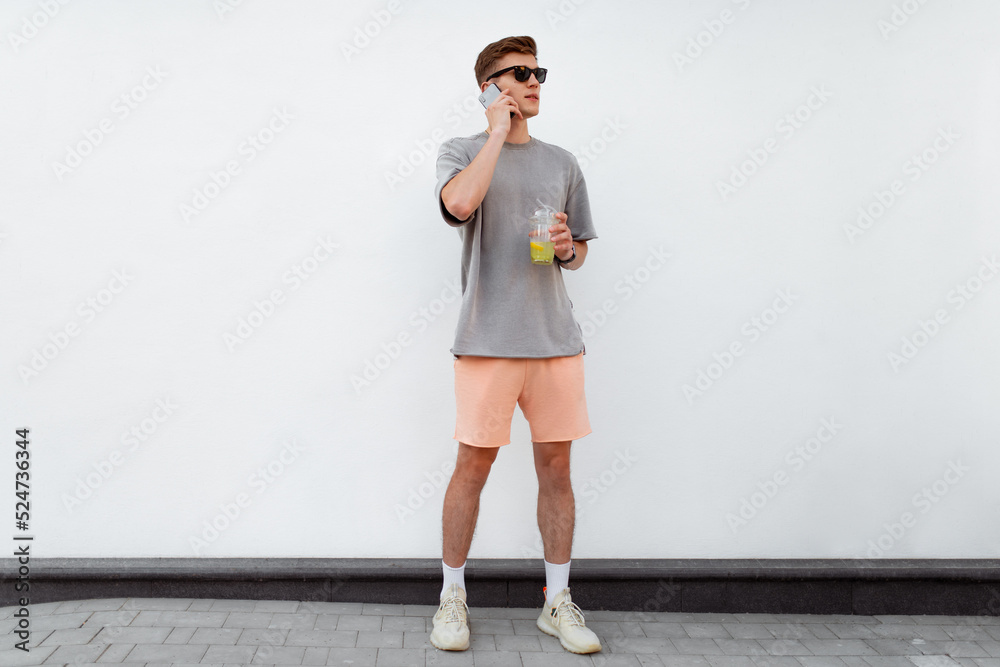Portrait of handsome confident stylish hipster man in sunglasses talking on the phone, standing guy near the concrete wall. Calm relaxing moment, summer vacation concept Portrait of handsome confident stylish hipster man in sunglasses talking on the phone, standing guy near the concrete wall. Calm relaxing moment, summer vacation concept