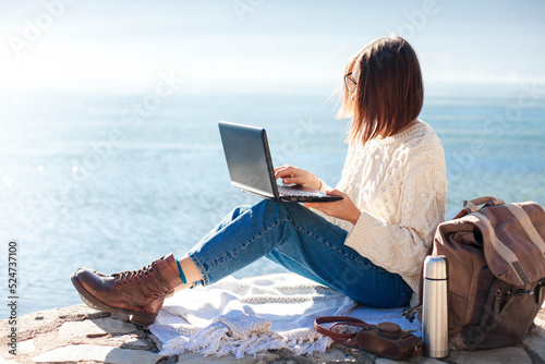 Freelancer workplace at sea beach. Young woman working in traveling from office at nature. Girl using laptop, Internet on pier outdoors. Female student in online education. Digital nomad in workation