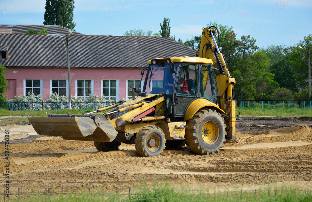 a yellow tractor with a blade and a bucket levels the sand at a construction site. construction machinery doing hard work a yellow tractor with a blade and a bucket levels the sand at a construction site. construction machinery doing hard work