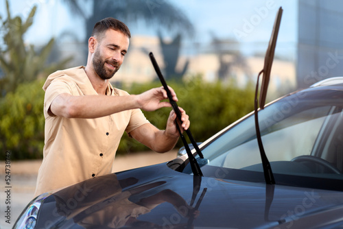 Foto Handsome latin man replace windshield wipers on car standing outdoors