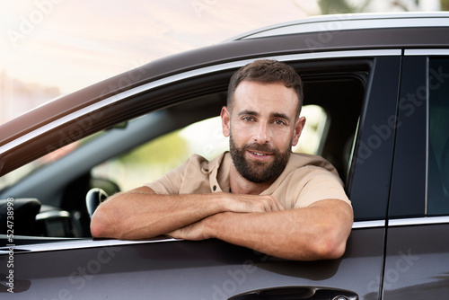 Portrait of handsome smiling latin driving sitting in car looking at camera. Transportation concept. Successful middle aged man buying new car in auto salon 