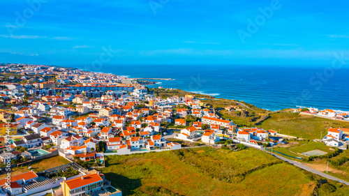 Drone view of a beautiful European city with a hilly landscape on ocean background. Aerial view of a small European town against blue sky and Atlantic Ocean. Beautiful natural landscape. Portugal.