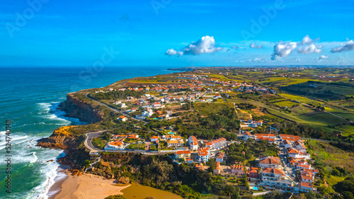 Aerial view of a small European town against blue sky and Atlantic Ocean. Drone view of a beautiful European city with a hilly landscape on ocean background. Beautiful natural landscape. Portugal. © Valua Vitaly