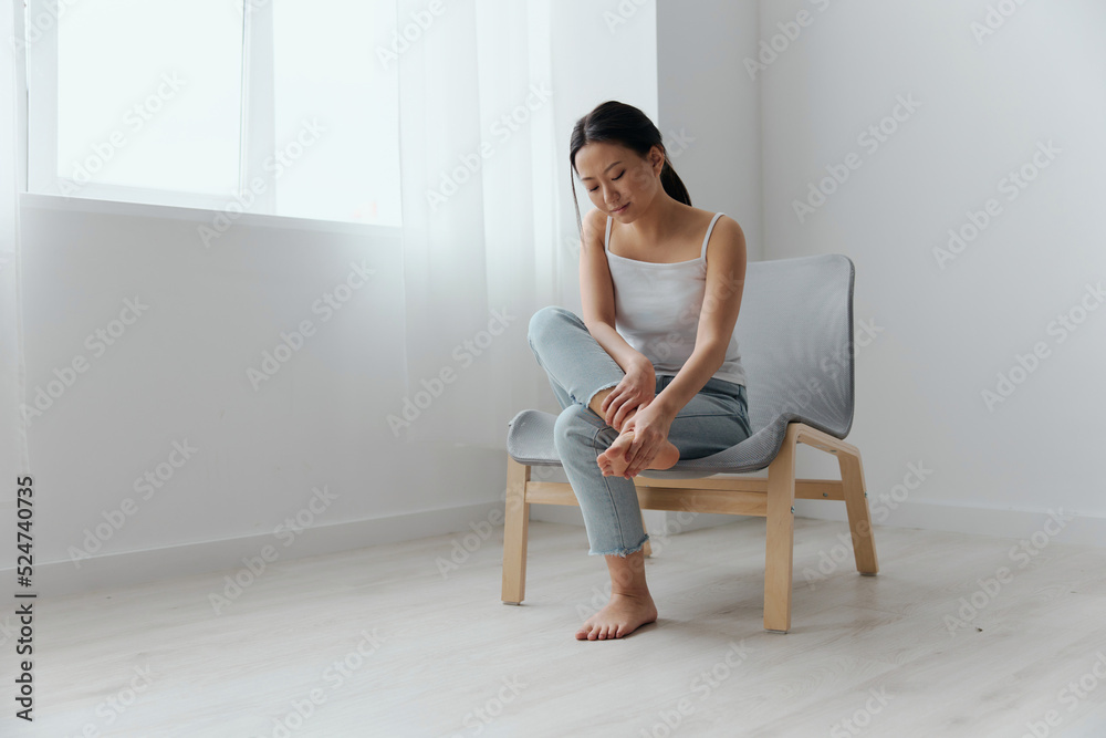 Full body shot suffering tanned beautiful young Asian woman touch pain foot massaging feet at home interior living room. Injuries Poor health Illness concept. Cool offer Banner Full body shot suffering tanned beautiful young Asian woman touch pain foot massaging feet at home interior living room. Injuries Poor health Illness concept. Cool offer Banner