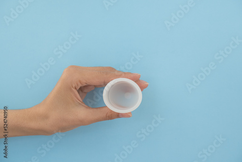 Close-up of a woman's hand holding a menstrual cup against a blue background. Women's health concept, zero waste alternatives.