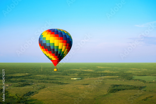 A colorful air balloon is flying in free flight over the field. Bird's-eye view. Multi colored balloon in the blue sky © Vera