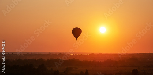 Colorful air balloon is flying in free flight over the field. Bird's-eye view. Multicolored balloon in the sky at sunset