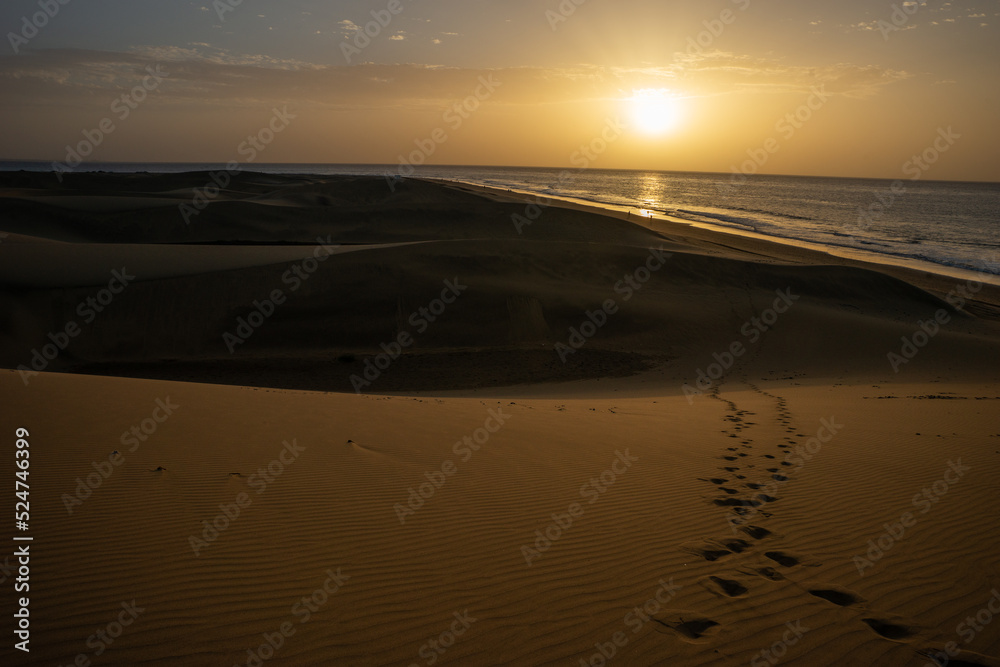 Footsteps in the sand with dunes and sunset