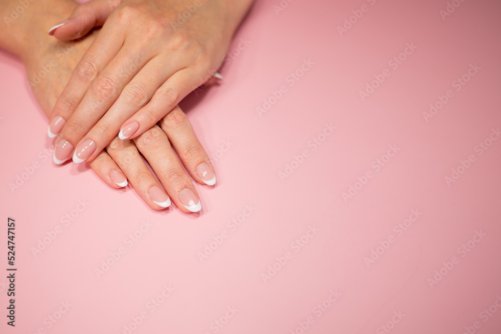female hands with beautiful classic french white manicure. Fingers isolated on a pastel pink background.
