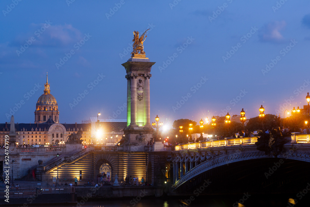 Naklejka premium Pont Alexandre III Bridge and illuminated lamp posts at sunset with view of the Invalides. 7th Arrondissement, Paris, France