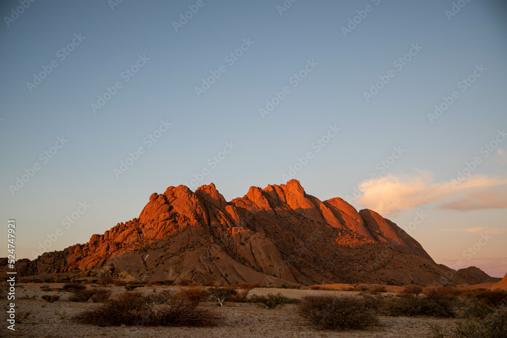 sun setting on red rock mountains in namibia desert