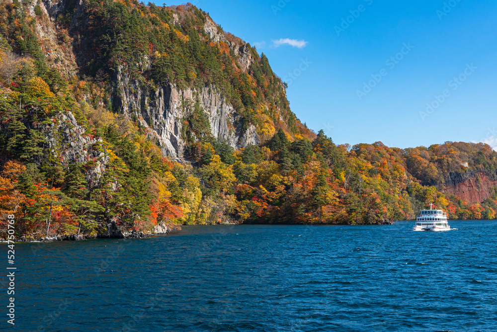 Lake Towada Sightseeing Cruises. Beautiful view, clear blue sky, white cloud, cruise ship in sunny day with autumn foliage season background. Aomori, Japan. Text in Japanese on ship 