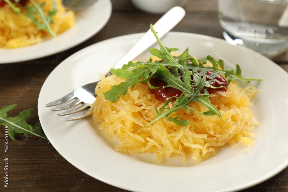 Tasty spaghetti squash with tomato sauce and arugula served on wooden table, closeup Tasty spaghetti squash with tomato sauce and arugula served on wooden table, closeup