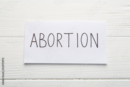 Paper note with word Abortion on white wooden background, top view