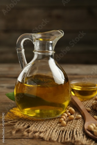 Glass jug with oil and soybeans on wooden table