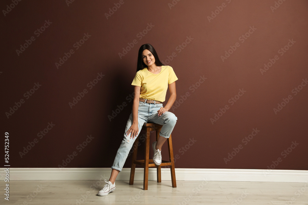 Beautiful young woman sitting on stool near brown wall Beautiful young woman sitting on stool near brown wall