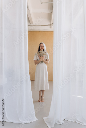 Girl in a linen dress and dried flowers near a white wall