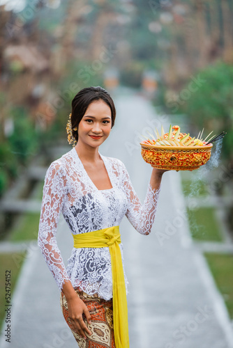 beautiful balinese woman wearing traditional kebaya in the penglipuran bali village smiling while carrying offering for praying photo